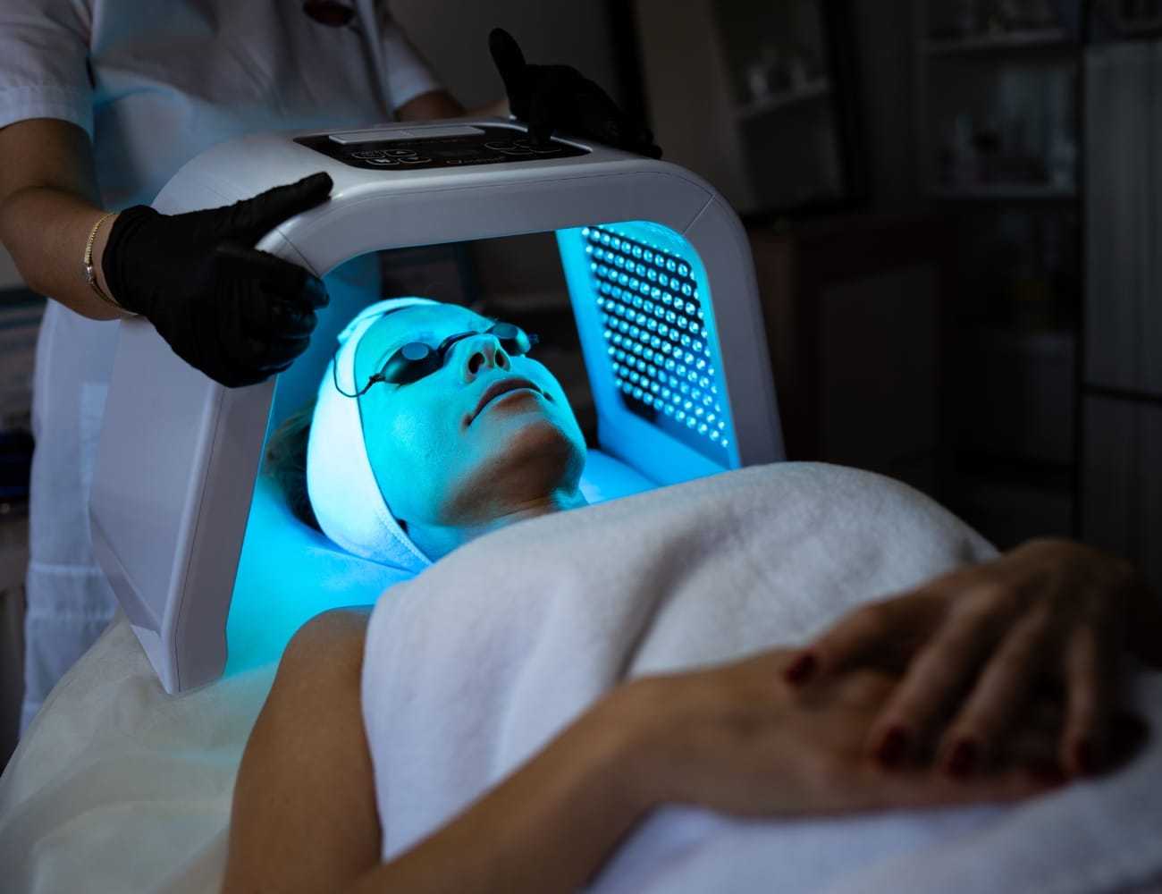 Person receiving LED light therapy under blue light device in spa setting.
