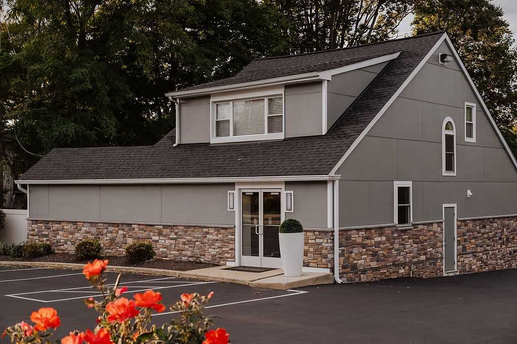 Modern gray house with stone accents, large windows, and vibrant flowers in the foreground.